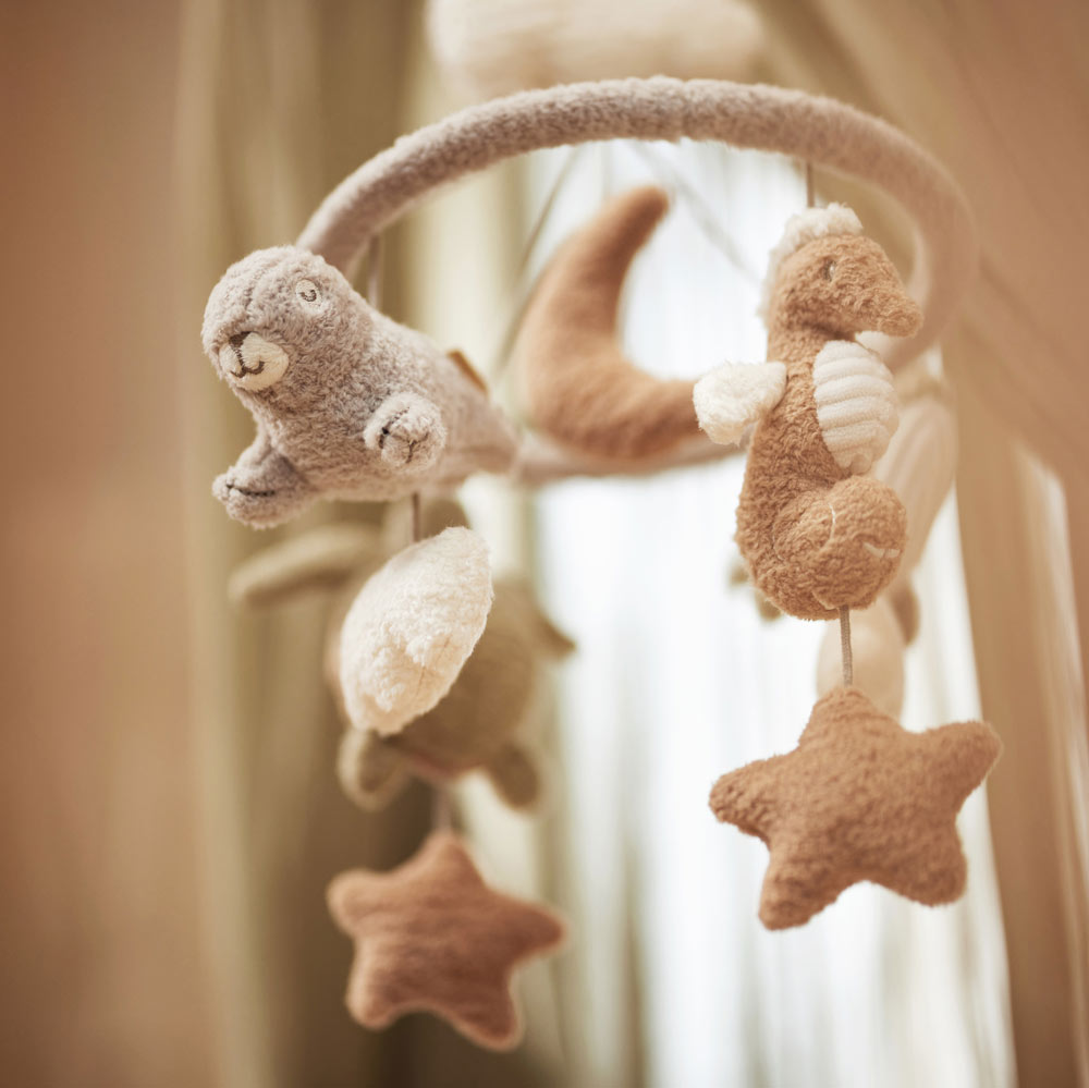 Mobile in sanften Tönen über dem Babybett mit Teddystoff