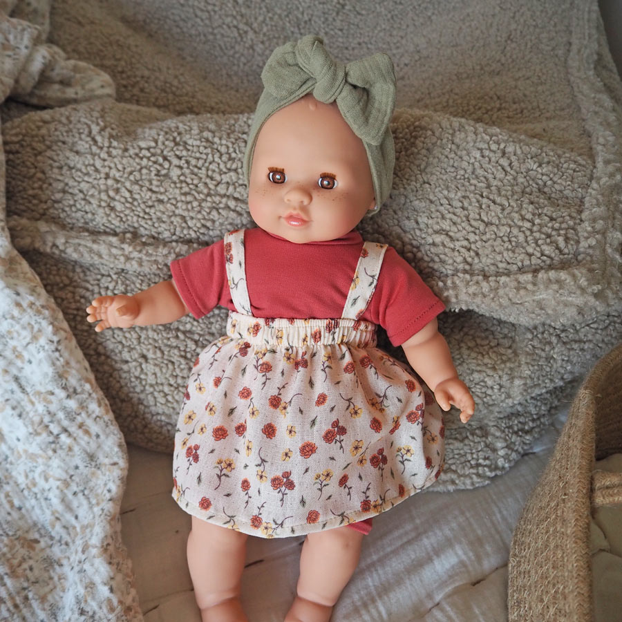 Spielzeugpuppe Julia mit rotem Shirt und roter Hose und einem Kleid in beige mit Blümchen und grünem Stirnband