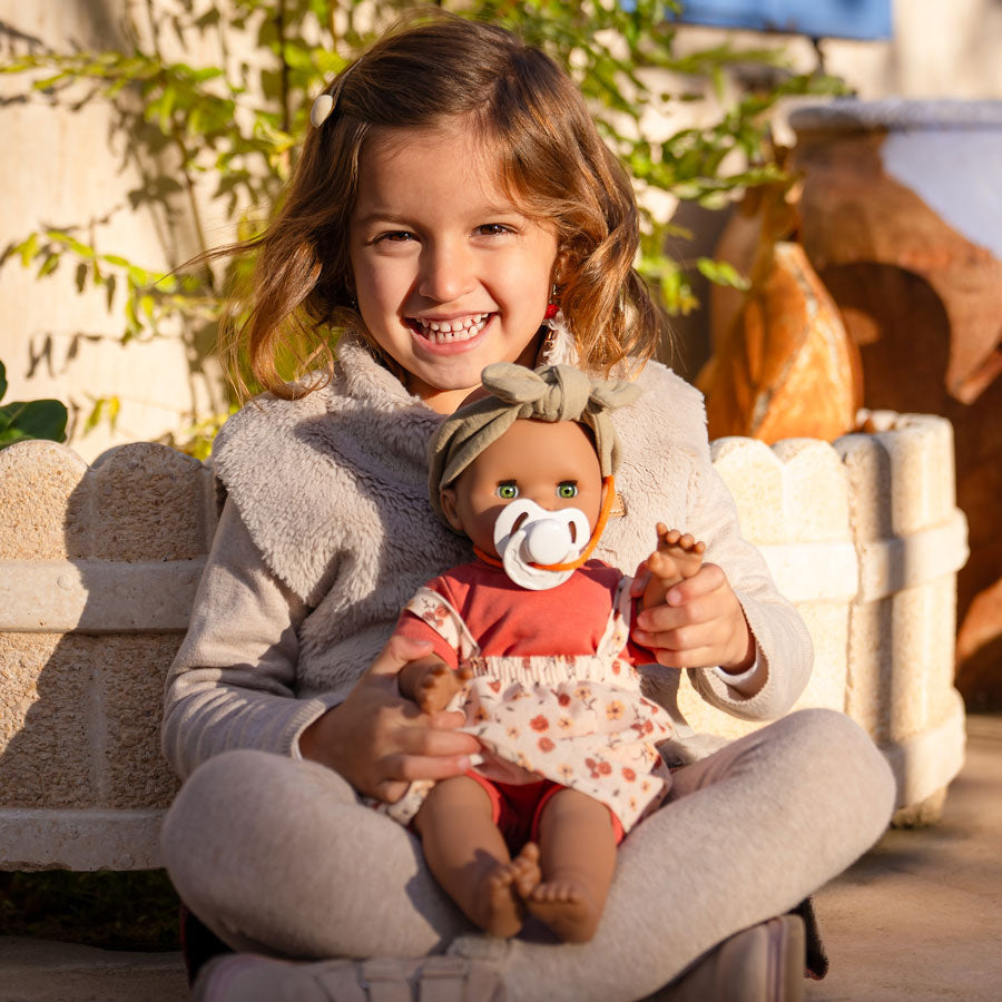 Mädchen spielt mir der Puppe Maja von Paola Reina draußen. Die Puppe hat leuchtend grüne Augen im Sonnenschein