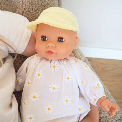 Die Puppe trägt eine gelbe Mütze und Hose und ein weißes Oberteil mit Gänseblümchen