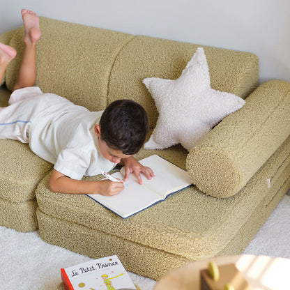 Junge liegt auf dem Bauch auf dem Kindersofa von Wigiwama und schreibt in einem Heft. Perfekt zum Erinnerungen sammeln. 