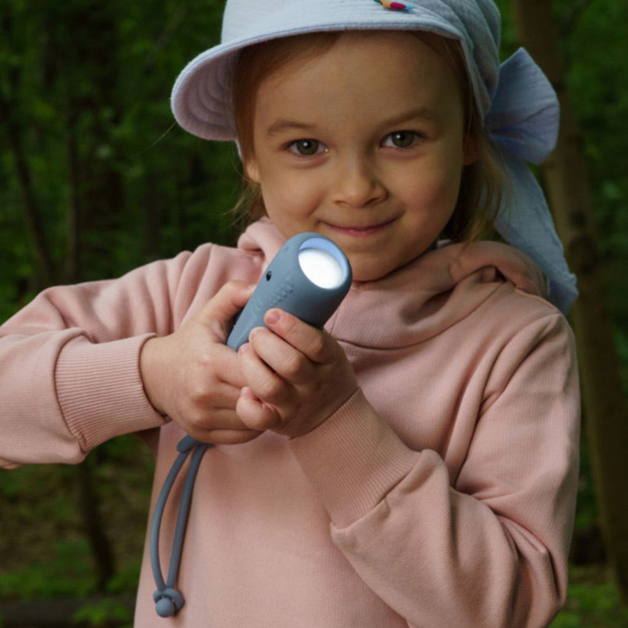 Mädchen leuchtet mit der Kinder-Taschenlampe Hai draußen im Wald